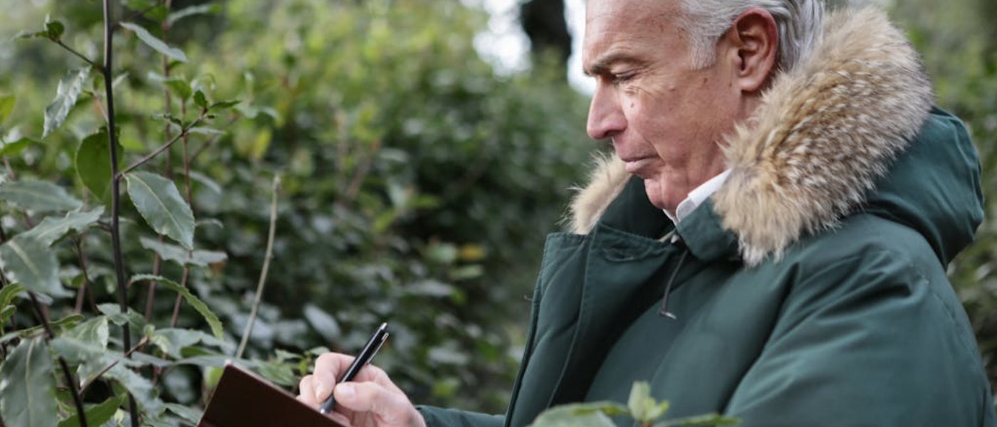 An older man wearing a warm jacket writes in his notebook