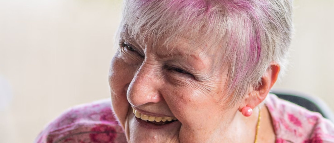 An older woman with pink dyed hair laughs