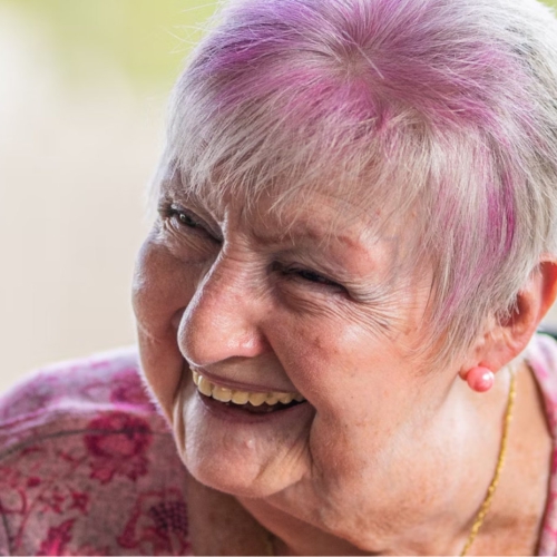 An older woman with pink dyed hair laughs