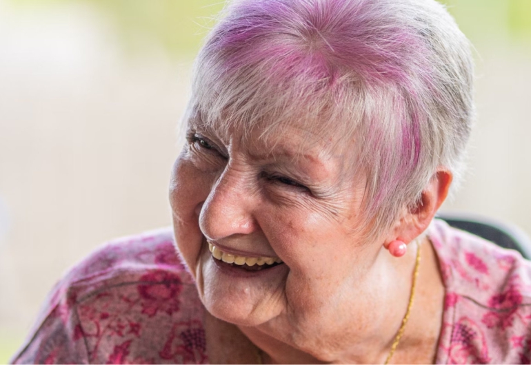 An older woman with pink dyed hair laughs