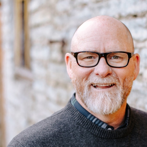 An older man wearing glasses smiles at the camera