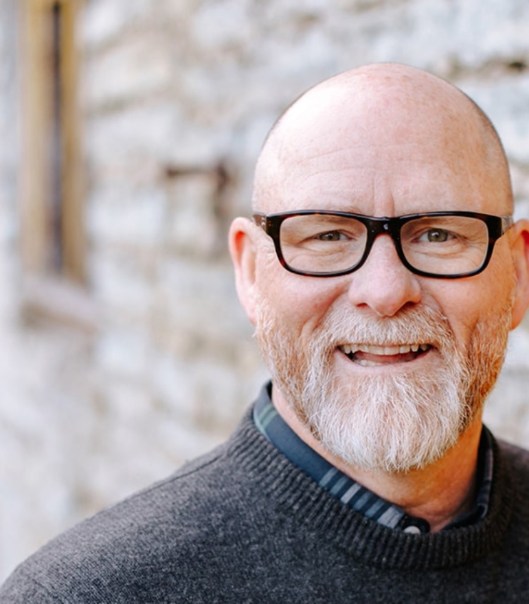 An older man wearing glasses smiles at the camera