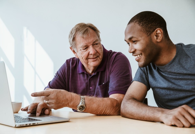 A man with a younger man looking at a laptop and smiling.