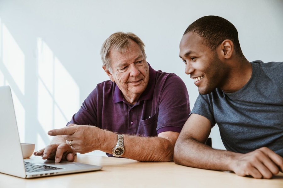 A man with a younger man looking at a laptop and smiling.